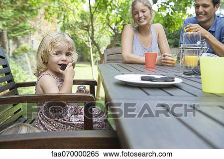 Little girl eating snack with her parents outdoors View Large Photo Image Stock Photography - Little girl eating snack with her parents outdoors. Fotosearch