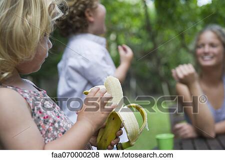 Little girl outdoors with her family, eating banana View Large Photo Image Stock Photo - Little girl outdoors with her family, eating banana. Fotosearch