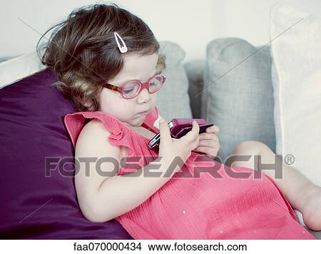 Little girl reclining on couch looking at cell phone View Large Photo Image Picture - Little girl reclining on couch looking at cell phone. Fotosearch