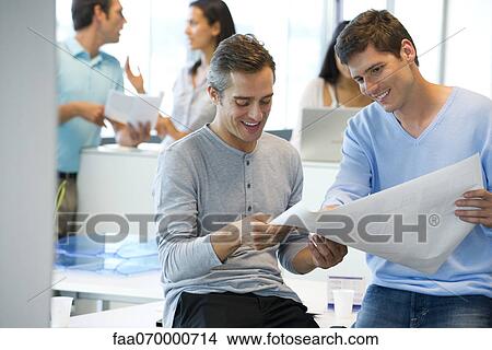 Picture - Male colleagues looking at blueprint together. Fotosearch