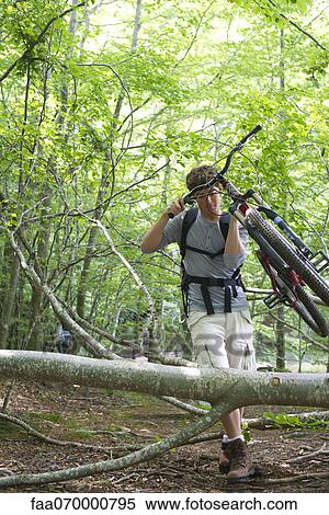 Stock Photography - Man carrying mountain bike in woods with fallen tree trunks. Fotosearch