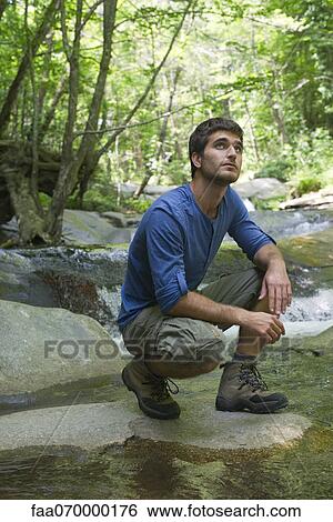 Man crouching by stream in woods View Large Photo Image Stock Photograph - Man crouching by stream in woods. Fotosearch