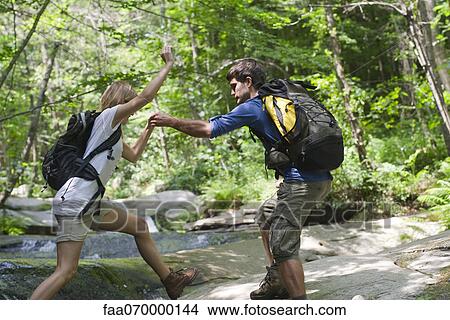 Picture - Man helping woman crossing stream. Fotosearch