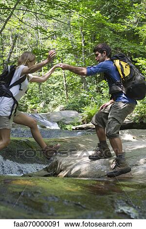 Stock Image - Man helping woman crossing stream. Fotosearch