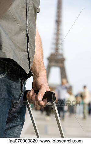 Man holding handle of rolling suitcase, Eiffel Tower visible in background, Paris, France View Large Photo Image Stock Image - Man holding handle of rolling suitcase, Eiffel Tower visible in background, Paris, France. Fotosearch