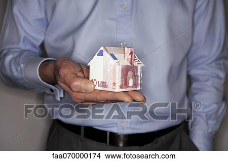 Picture - Man holding model house folded with euro banknote, mid section. Fotosearch