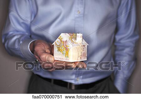 Stock Image - Man holding model house folded with British pound banknote, mid section. Fotosearch