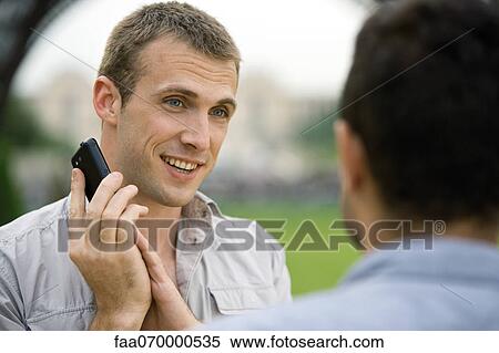 Stock Photography - Man on phone call, covering cellphone mouthpiece with hand to talk to acquaintance. Fotosearch