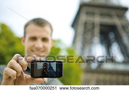 Stock Image - Man photographing himself in front of Eiffel Tower, Paris, France. Fotosearch