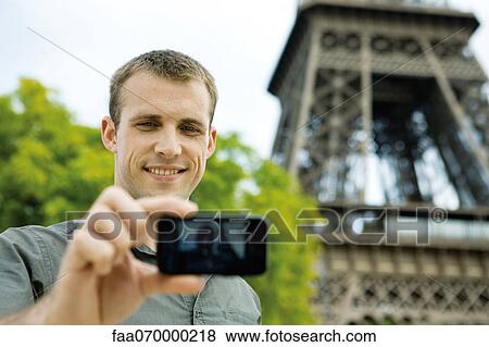 Stock Photo - Man photographing himself in front of Eiffel Tower, Paris, France. Fotosearch