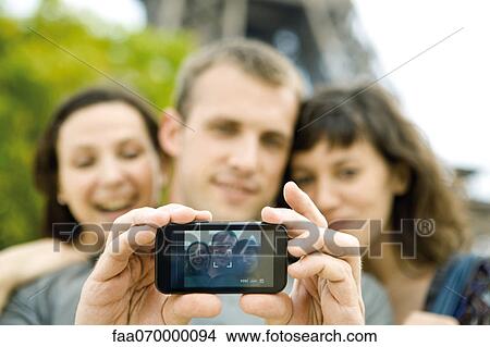 Man photographing himself with two female friends using cell phone View Large Photo Image Picture - Man photographing himself with two female friends using cell phone. Fotosearch