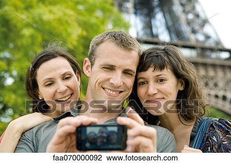Man photographing himself with two female friends using cell phone View Large Photo Image Stock Image - Man photographing himself with two female friends using cell phone. Fotosearch