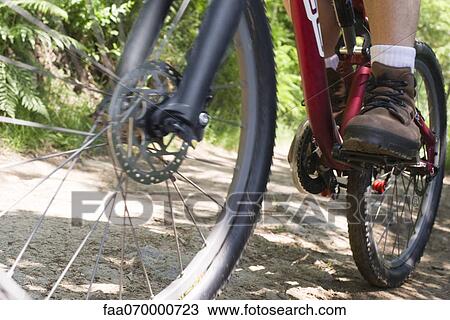 Stock Image - Man riding bicycle on dirt road, low section. Fotosearch