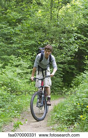 Stock Image - Man riding bicycle through woods. Fotosearch