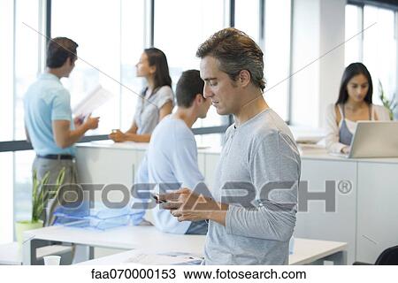 Man text messaging with cell phone in office View Large Photo Image Stock Image - Man text messaging with cell phone in office. Fotosearch