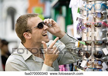 Man trying on sunglasses in street market View Large Photo Image Stock Image - Man trying on sunglasses in street market. Fotosearch