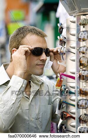 Man trying on sunglasses in street market View Large Photo Image Stock Photograph - Man trying on sunglasses in street market. Fotosearch