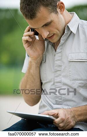 Stock Photo - Man using cell phone and digital tablet outdoors. Fotosearch