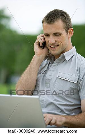 Stock Photograph - Man using cell phone and laptop computer outdoors. Fotosearch