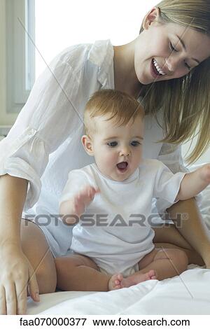 Stock Photo - Mother and baby playing on bed. Fotosearch