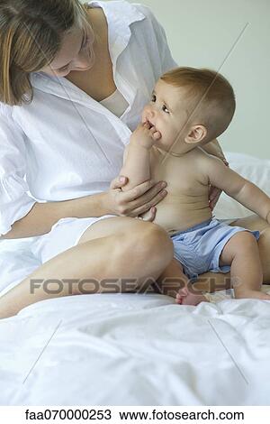 Stock Image - Mother and baby sitting together on bed. Fotosearch