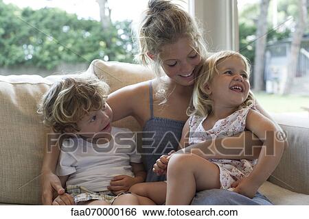 Stock Photograph - Mother and two young children cuddling on sofa. Fotosearch