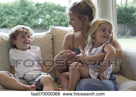 Mother and two young children sitting together on sofa View Large Photo Image Stock Photo - Mother and two young children sitting together on sofa. Fotosearch