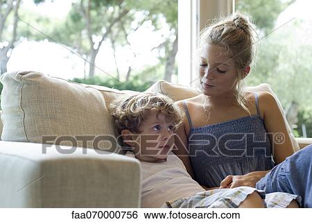 Stock Photograph - Mother and young son sitting together on sofa. Fotosearch