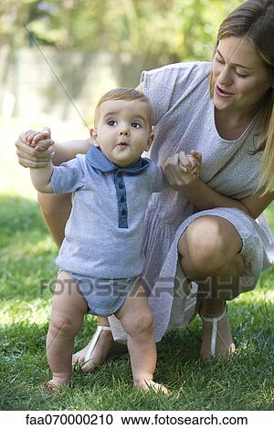 Stock Image - Mother helping baby stand outdoors. Fotosearch