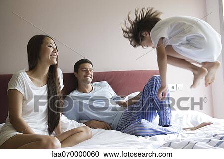 Parents watching as young son jumps on bed View Large Photo Image Stock Image - Parents watching as young son jumps on bed. Fotosearch