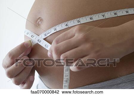 Stock Image - Pregnant woman measuring her belly with measuring tape, cropped. Fotosearch