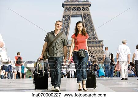 Stock Photo - Tourist couple walking with their luggage near Eiffel Tower, Paris, France. Fotosearch