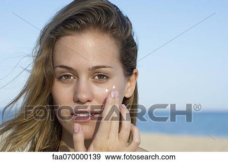 Stock Photo - Woman applying sunscreen at the beach, portrait. Fotosearch