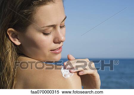 Stock Photography - Woman applying sunscreen at the beach. Fotosearch