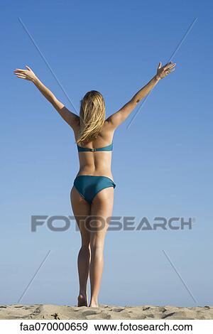 Stock Photo - Woman at the beach with arms raised in air, rear view. Fotosearch