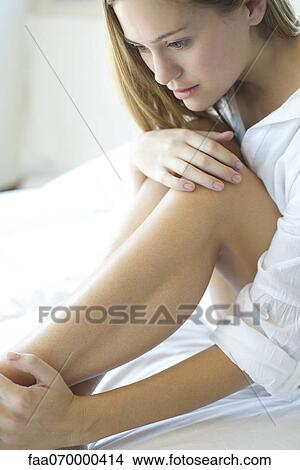 Picture - Woman daydreaming, touching bare legs. Fotosearch