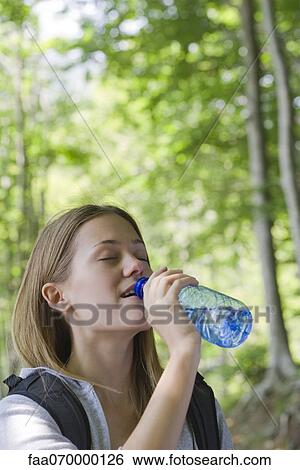 Woman drinking bottled water in woods View Large Photo Image Stock Photograph - Woman drinking bottled water in woods. Fotosearch