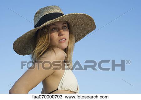 Stock Image - Woman in bikini and sunhat looking away in thought, portrait. Fotosearch