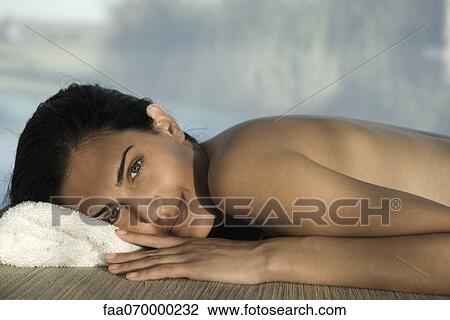 Stock Image - Woman lying on stomach at spa, smiling at camera, waist up. Fotosearch