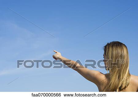 Stock Photograph - Woman pointing at the sky, rear view. Fotosearch