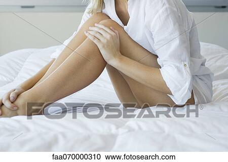 Stock Image - Woman relaxing on bed, touching bare legs. Fotosearch