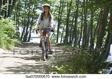 Stock Image - Woman riding bicycle in woods. Fotosearch