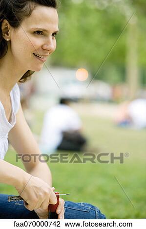 Stock Image - Woman uncorking wine bottle outdoors. Fotosearch
