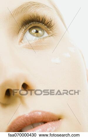 Stock Image - Woman with dots of undereye cream applied beneath eye, extreme close-up, cropped. Fotosearch