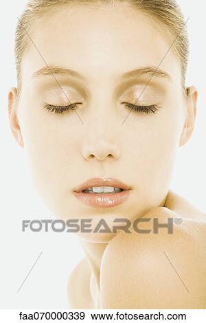 Stock Photo - Woman with eyes closed, wearing natural cosmetics, resting chin on shoulder. Fotosearch