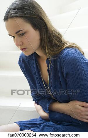 Young woman clutching stomach, looking down in thought View Large Photo Image Picture - Young woman clutching stomach, looking down in thought. Fotosearch