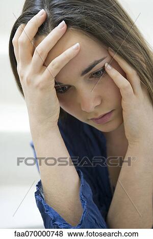 Stock Photo - Young woman holding head and looking down. Fotosearch