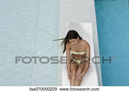 Young woman sitting on deckchair by pool View Large Photo Image Stock Photo - Young woman sitting on deckchair by pool. Fotosearch
