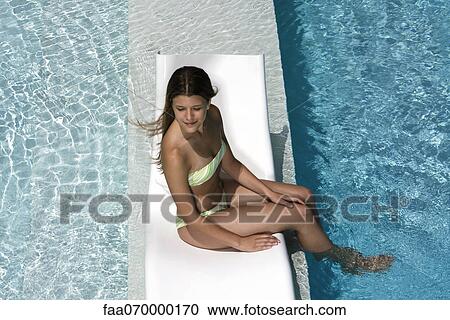 Young woman sitting on poolside deckchair dangling feet into water View Large Photo Image Stock Image - Young woman sitting on poolside deckchair dangling feet into water. Fotosearch