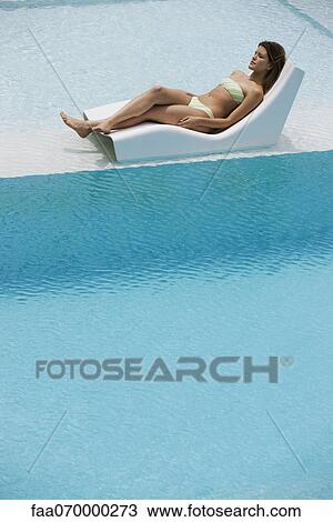 Stock Image - Young woman sunbathing by pool. Fotosearch